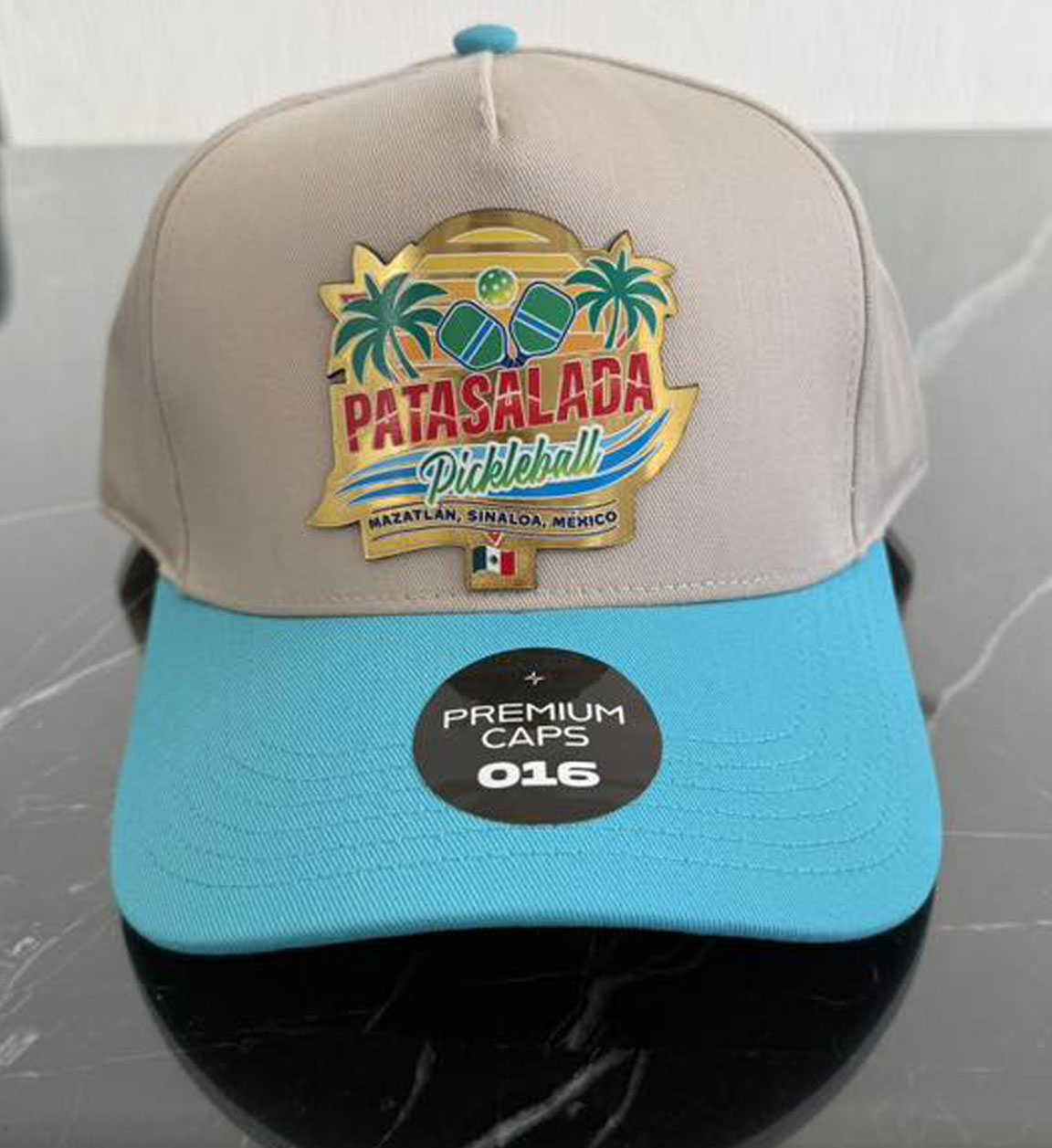 A tan and light blue snapback baseball cap featuring a "Pata Salada Pickleball" embroidered patch with palm trees, paddles, and the Mexican flag.
