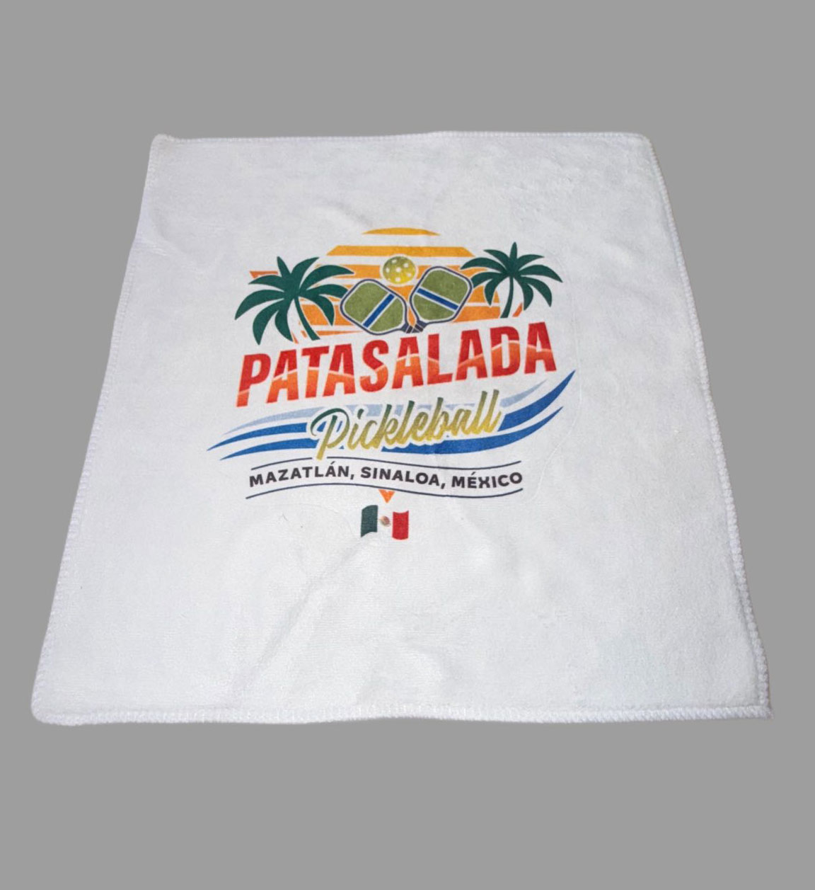 A white rectangular sports towel featuring a large "Pata Salada Pickleball" logo with two crossed paddles, palm trees, a yellow pickleball sunset, and a small Mexican flag